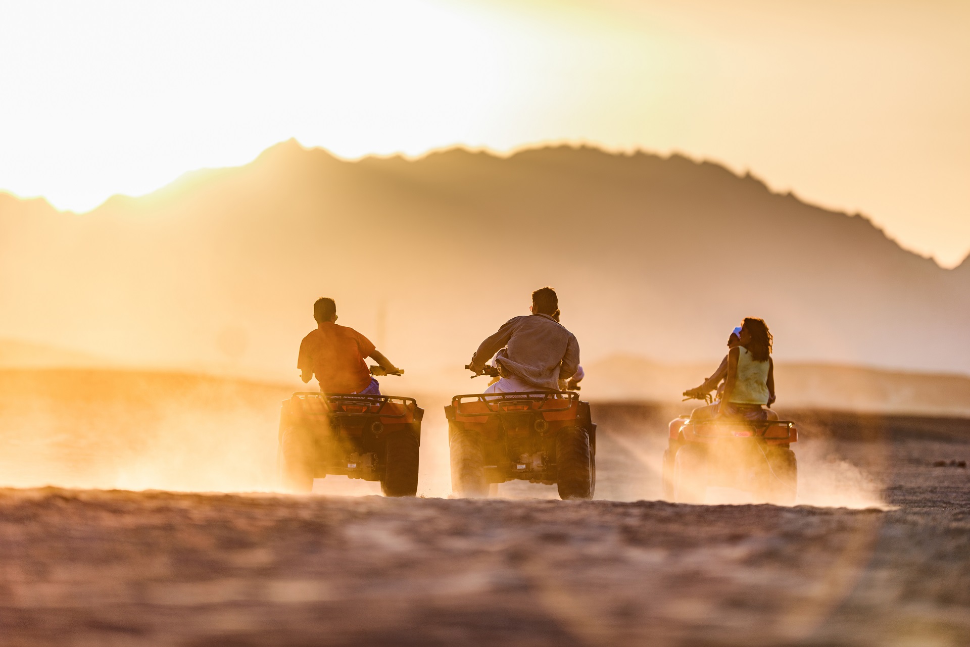 Back view of group of people driving quad bikes in the desert at sunset. Copy space.