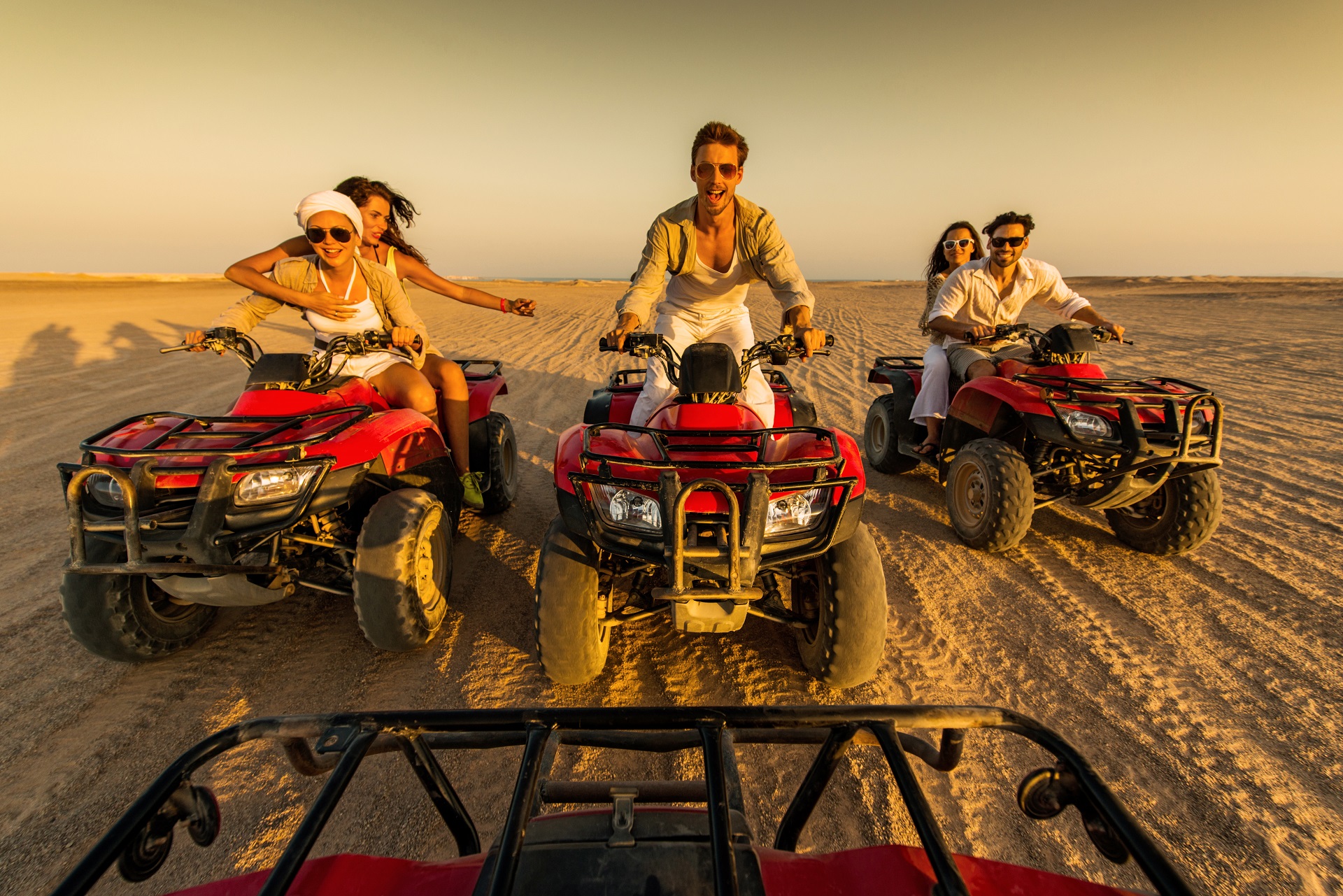Group of young people having fun in the desert while driving on quad bikes.