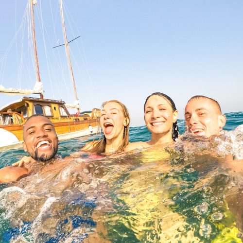 Young multiracial friends taking selfie and swimming on sailing boat sea trip - Rich happy guys and girls having fun in summer party day - Exclusive vacation concept - Bright afternoon  warm filter